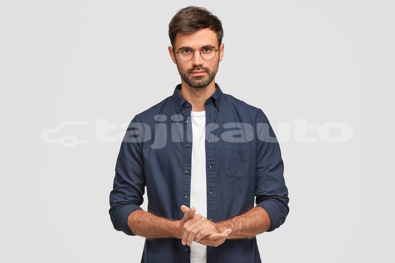 Big with watermark waist up portrait handsome serious unshaven male keeps hands together dressed dark blue shirt has talk with interlocutor stands against white wall self confident man freelancer