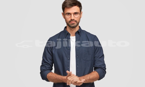 Medium with watermark waist up portrait handsome serious unshaven male keeps hands together dressed dark blue shirt has talk with interlocutor stands against white wall self confident man freelancer